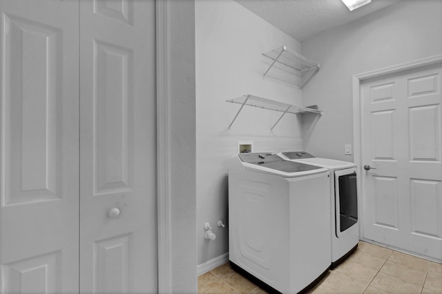 laundry area featuring a textured ceiling, washing machine and dryer, and light tile patterned floors