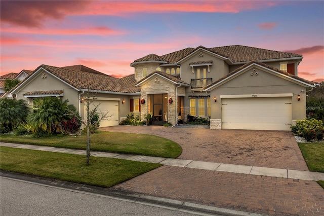 mediterranean / spanish house featuring a garage, a balcony, stone siding, decorative driveway, and stucco siding