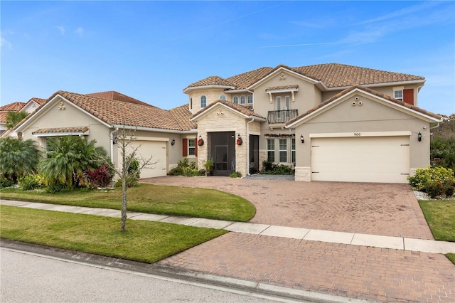 mediterranean / spanish-style house with a balcony, a tile roof, an attached garage, decorative driveway, and stucco siding