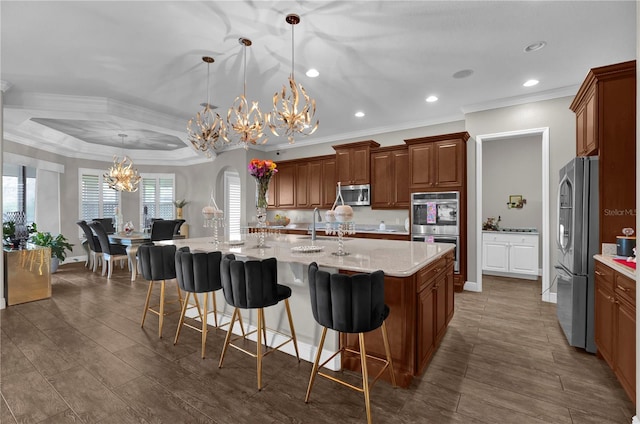 kitchen featuring decorative light fixtures, appliances with stainless steel finishes, brown cabinetry, a kitchen island with sink, and a kitchen breakfast bar