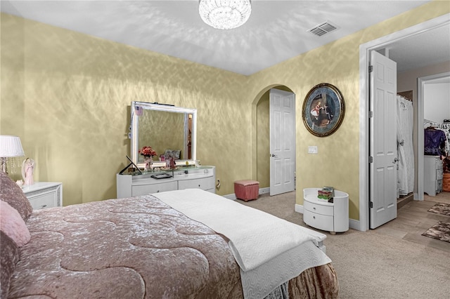 carpeted bedroom featuring baseboards, visible vents, arched walkways, and a chandelier