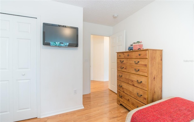 bedroom with a closet, a textured ceiling, and light hardwood / wood-style flooring