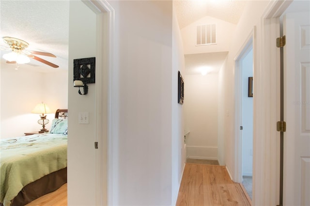 hall with lofted ceiling, light hardwood / wood-style flooring, and a textured ceiling