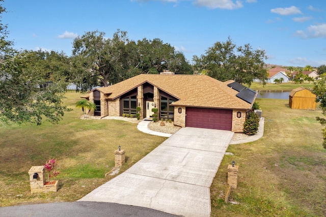 view of front of home with solar panels, a front lawn, a garage, and a water view