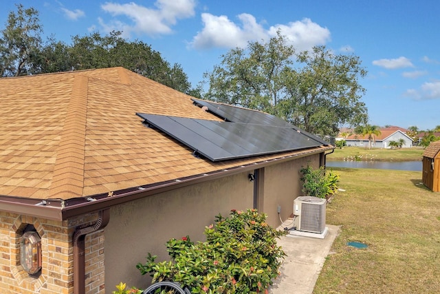 view of side of property with central AC, a yard, a water view, and solar panels