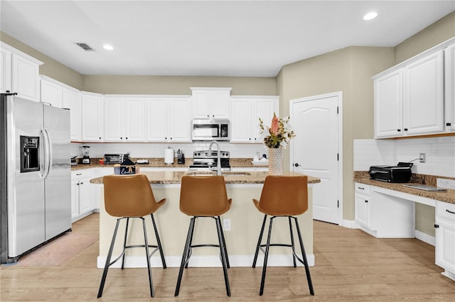 kitchen featuring a breakfast bar area, white cabinetry, light stone counters, appliances with stainless steel finishes, and an island with sink