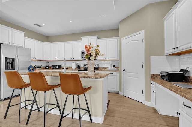 kitchen featuring white cabinetry, light stone countertops, stainless steel appliances, and an island with sink