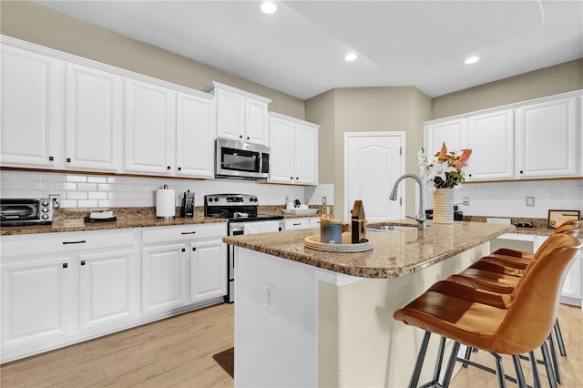 kitchen with white cabinetry, stainless steel appliances, a kitchen island with sink, and a breakfast bar area