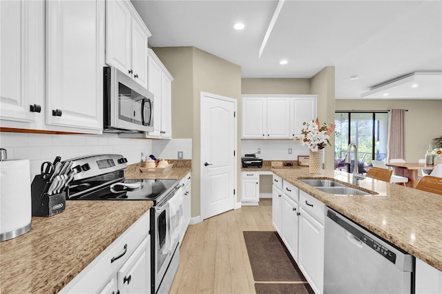 kitchen with sink, white cabinetry, light stone counters, light wood-type flooring, and stainless steel appliances