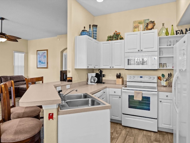 kitchen with white appliances, kitchen peninsula, a breakfast bar, white cabinets, and sink