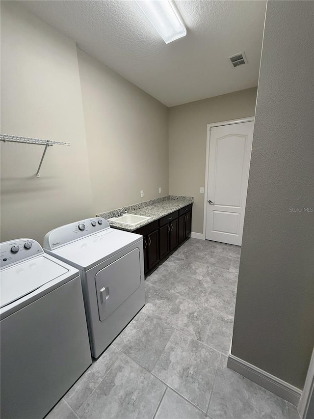 laundry area with a textured ceiling, cabinets, separate washer and dryer, and sink