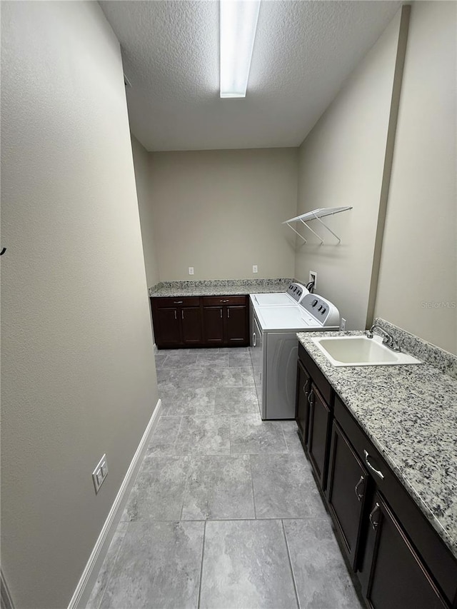 laundry area with a textured ceiling, cabinets, washer and dryer, and sink