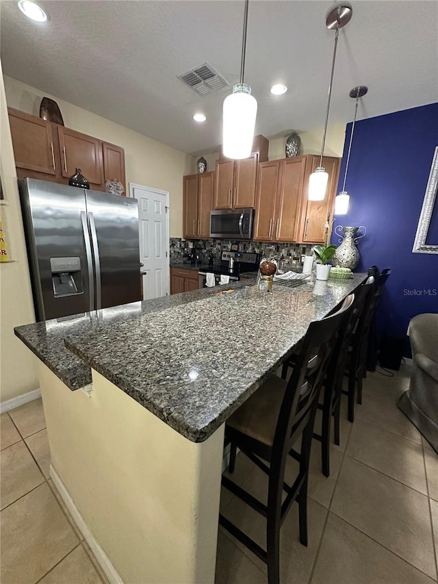 kitchen featuring hanging light fixtures, stainless steel appliances, backsplash, a breakfast bar area, and light tile patterned flooring