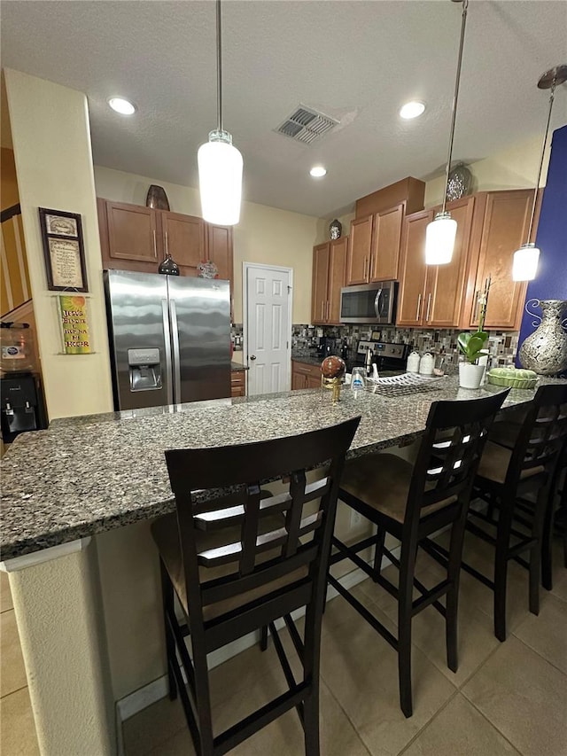 kitchen featuring hanging light fixtures, light tile patterned floors, appliances with stainless steel finishes, tasteful backsplash, and a breakfast bar area