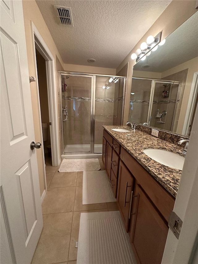 bathroom with a textured ceiling, vanity, a shower with door, tile patterned flooring, and toilet