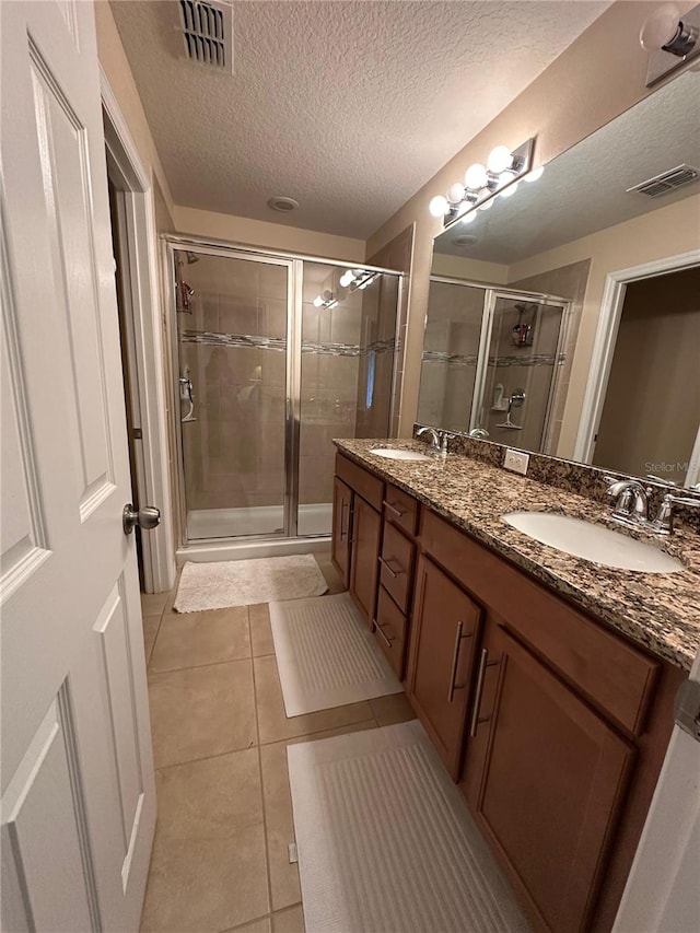 bathroom with tile patterned floors, vanity, an enclosed shower, and a textured ceiling