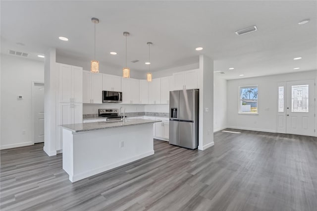 kitchen with light stone countertops, an island with sink, white cabinets, and stainless steel appliances