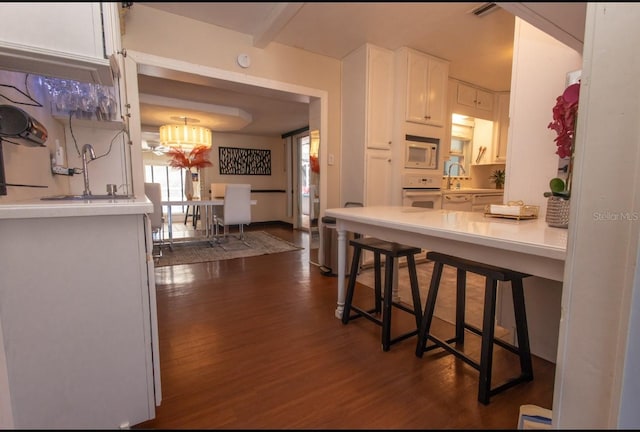 kitchen featuring sink, white appliances, dark wood-type flooring, a breakfast bar area, and white cabinetry