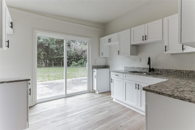 kitchen featuring stone counters, sink, a textured ceiling, light hardwood / wood-style floors, and white cabinetry