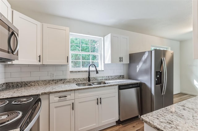 kitchen with light stone countertops, stainless steel appliances, sink, light hardwood / wood-style floors, and white cabinetry