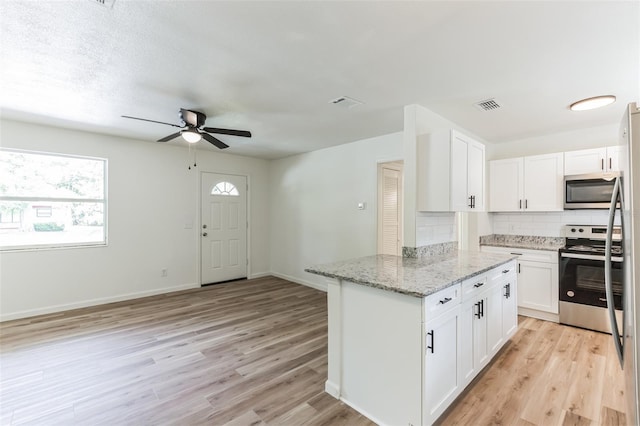 kitchen with light stone counters, light hardwood / wood-style floors, decorative backsplash, white cabinets, and appliances with stainless steel finishes