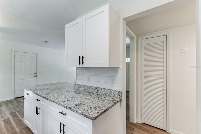 kitchen featuring white cabinets, decorative backsplash, light stone counters, and light hardwood / wood-style flooring