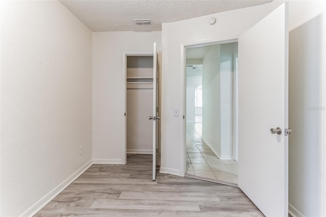 unfurnished bedroom featuring a closet, a textured ceiling, and light wood-type flooring