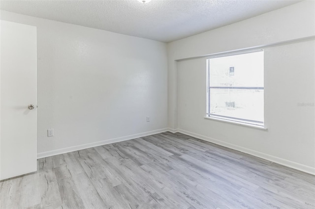 empty room with light wood-type flooring and a textured ceiling