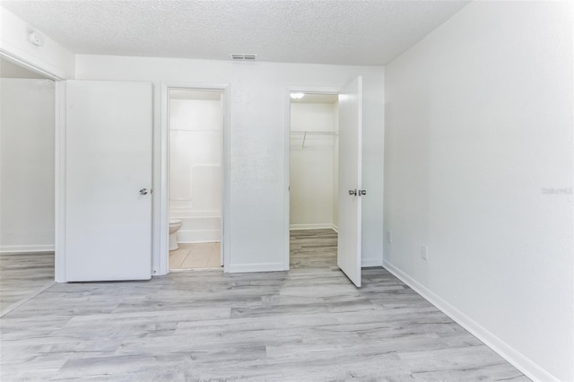 unfurnished bedroom with ensuite bathroom, a walk in closet, light hardwood / wood-style flooring, a textured ceiling, and a closet