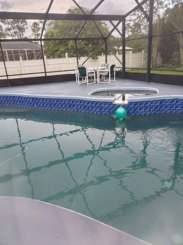 pool at dusk featuring glass enclosure, a patio area, and an in ground hot tub