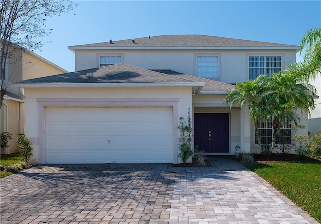 view of front of property featuring a garage, decorative driveway, roof with shingles, and stucco siding