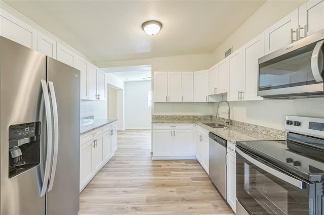 kitchen with light stone countertops, stainless steel appliances, white cabinetry, and sink