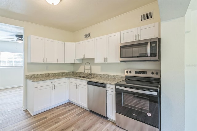 kitchen featuring white cabinets, sink, light stone countertops, appliances with stainless steel finishes, and light hardwood / wood-style floors