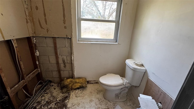 bathroom with toilet and concrete block wall