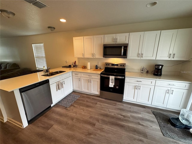 kitchen with appliances with stainless steel finishes, white cabinetry, sink, dark hardwood / wood-style flooring, and kitchen peninsula