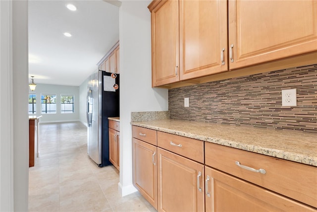 kitchen featuring decorative backsplash, light brown cabinetry, stainless steel refrigerator, and light stone countertops