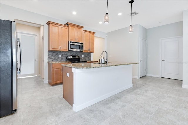 kitchen featuring light stone countertops, sink, decorative light fixtures, a kitchen island with sink, and appliances with stainless steel finishes