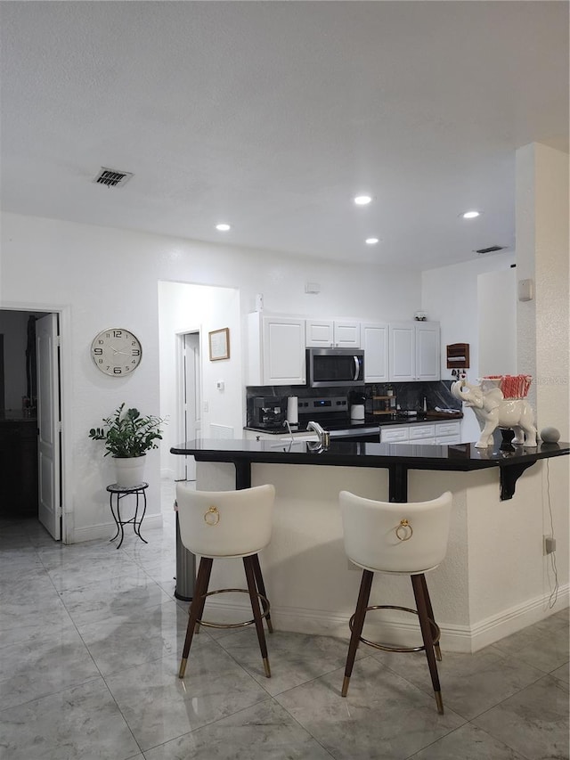 kitchen featuring a breakfast bar, kitchen peninsula, white cabinets, and stainless steel appliances