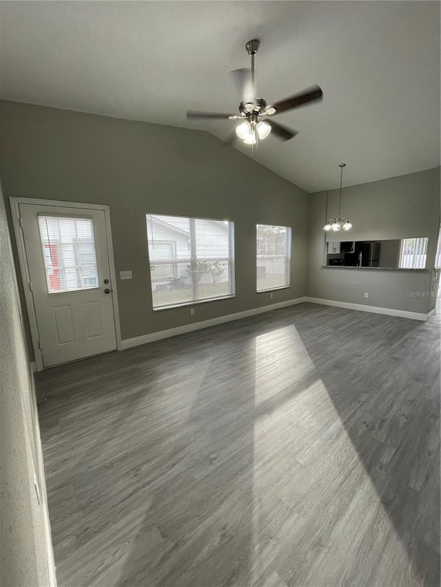 unfurnished living room featuring a wealth of natural light, ceiling fan with notable chandelier, dark wood-type flooring, and vaulted ceiling