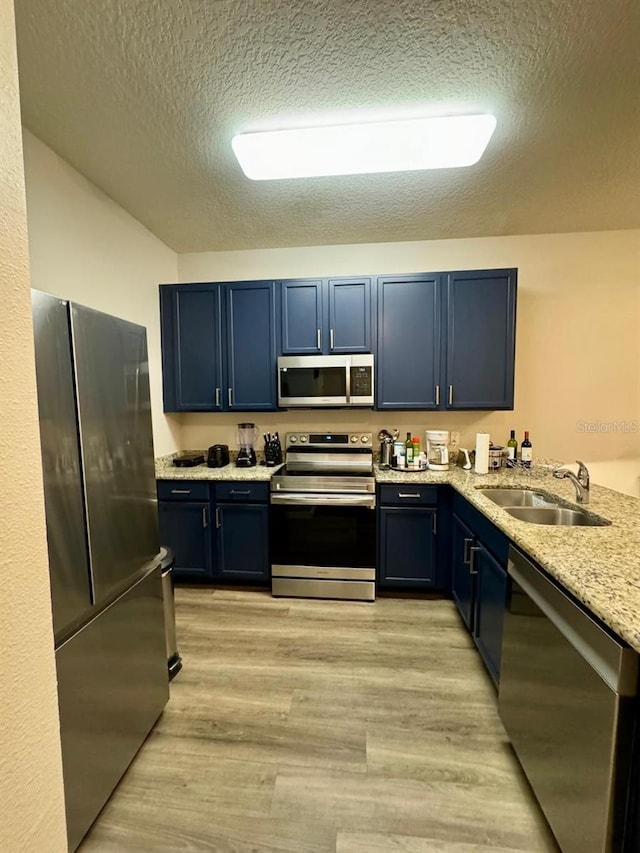 kitchen with sink, light stone countertops, light wood-type flooring, blue cabinetry, and appliances with stainless steel finishes