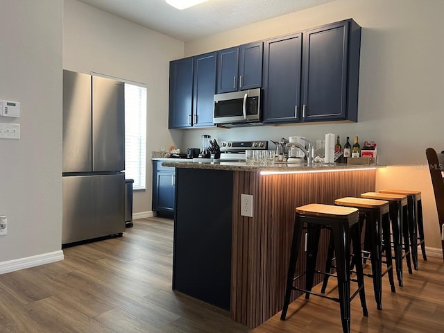 kitchen featuring blue cabinetry, stainless steel appliances, a kitchen breakfast bar, kitchen peninsula, and wood-type flooring