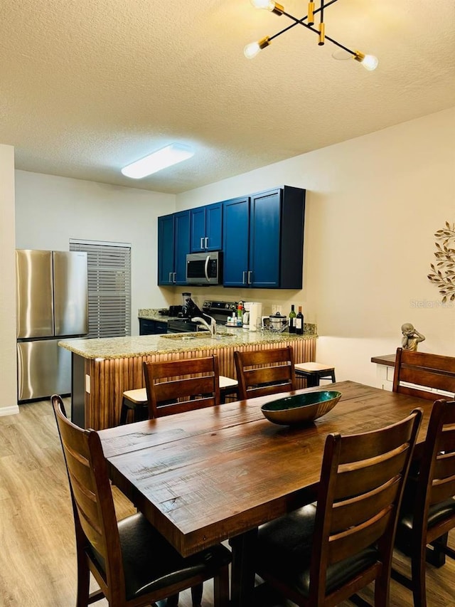 dining room with sink, a chandelier, a textured ceiling, and light wood-type flooring