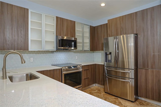 kitchen featuring backsplash, light stone countertops, sink, and appliances with stainless steel finishes