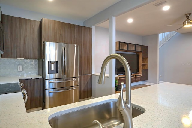 kitchen featuring light stone countertops, sink, ceiling fan, stainless steel appliances, and backsplash