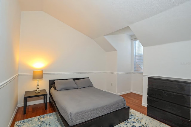 bedroom with wood-type flooring, a textured ceiling, and lofted ceiling