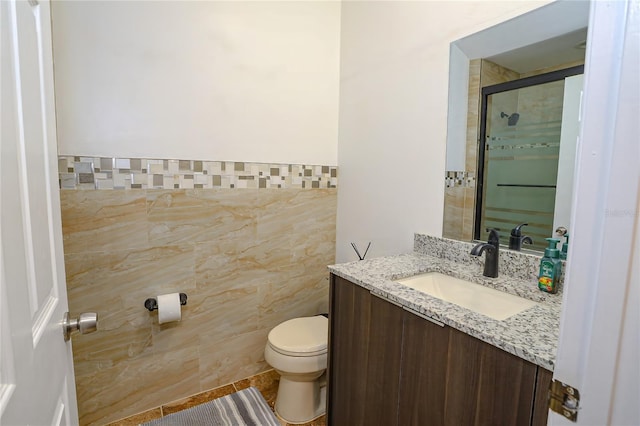 bathroom with vanity, a shower with door, tile patterned flooring, toilet, and tile walls