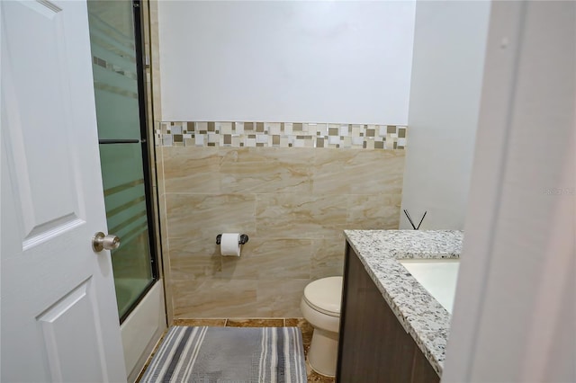 full bathroom featuring tile patterned floors, toilet, shower / bath combination with glass door, vanity, and tile walls