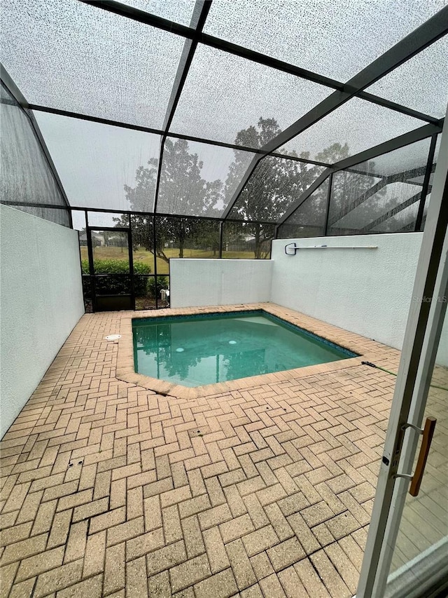 view of swimming pool featuring glass enclosure and a patio