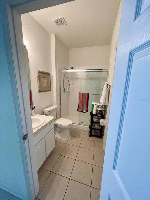 bathroom featuring a shower with shower door, toilet, vanity, and tile patterned flooring