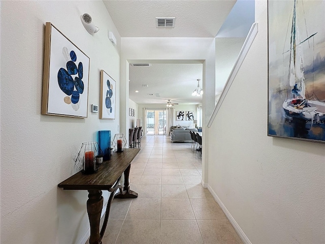 hall with a textured ceiling, light tile patterned floors, and an inviting chandelier